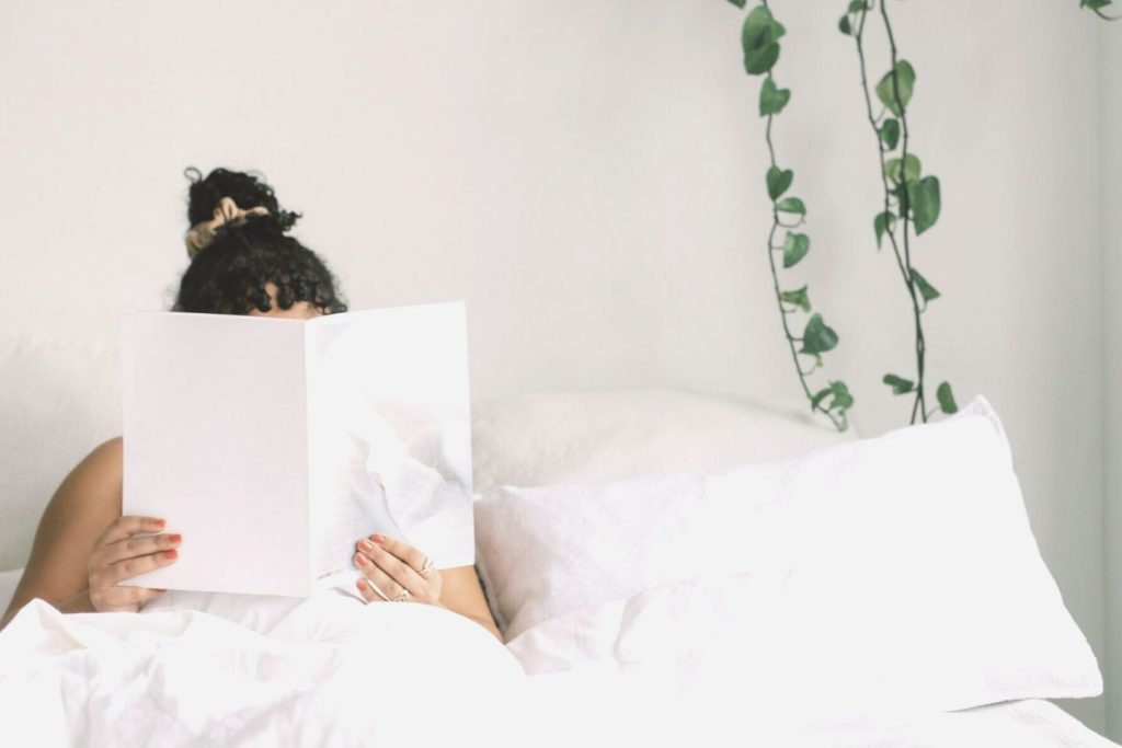 woman holding book on bed in front of face