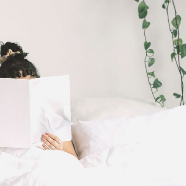 woman holding book on bed in front of face