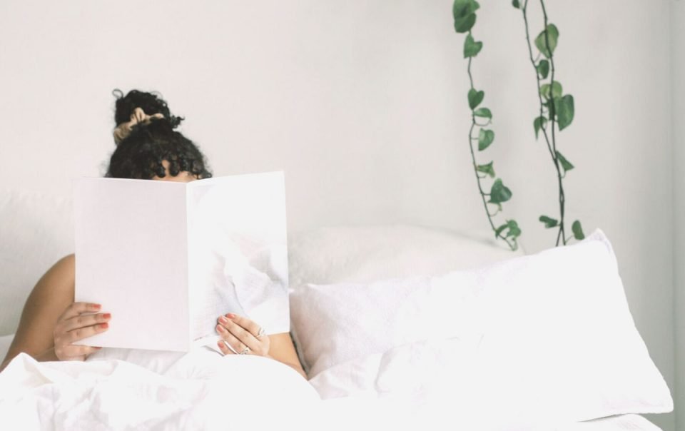 woman holding book on bed in front of face