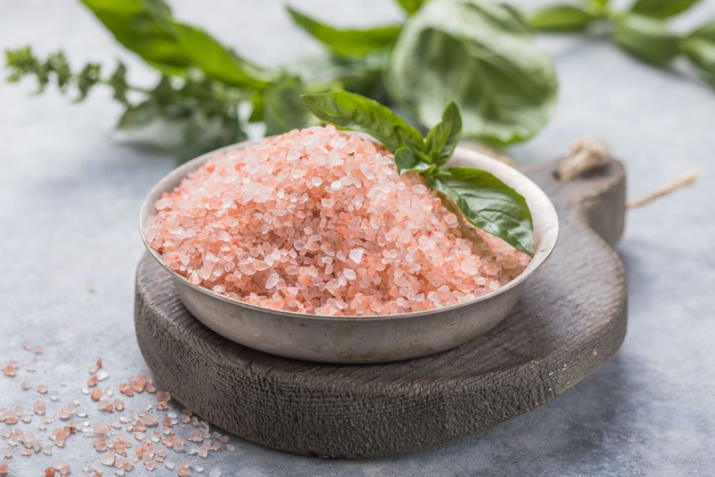 A bowl of pink salt with herbs on a table.